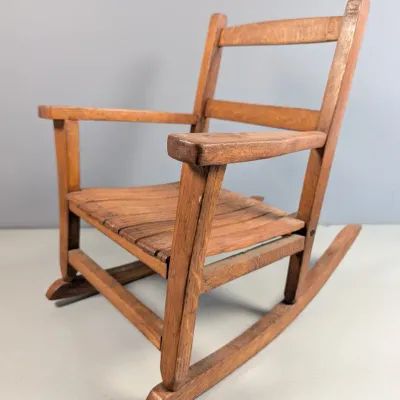 Sale Photo Thumbnail #165: Vintage child-sized wooden rocking chair with a slat seat and ladder-back design, showing rustic wear to the finish.