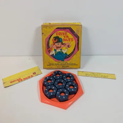Sale Photo Thumbnail #50: Vintage Milton Bradley "Drive Ya Nuts" puzzle game in its original box with blue numbered nuts and red tray.