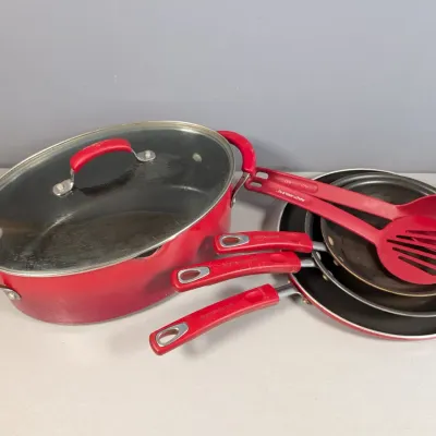 Sale Photo Thumbnail #25: Rachael Ray red nonstick cookware set featuring a covered oval pot, nested frying pans, and matching utensils.