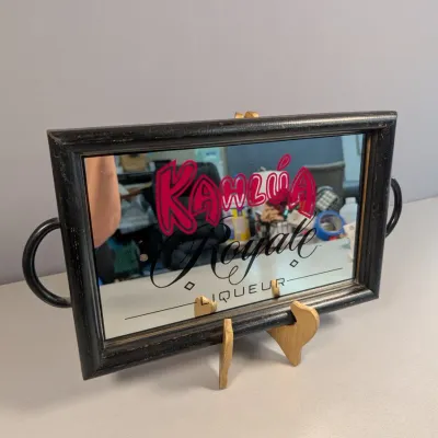 Sale Photo Thumbnail #132: Vintage Kahlúa Royale Liqueur advertising mirror serving tray in a black wooden frame with side metal handles, displayed on a wooden stand.