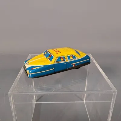 Sale Photo Thumbnail #412: Vintage lithographed tin toy taxi car in blue and yellow, featuring lithographed passengers and minor paint wear.