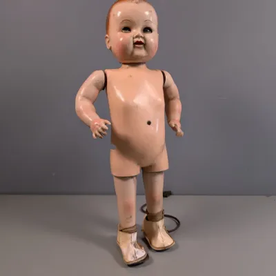 Sale Photo Thumbnail #333: Vintage composition standing baby doll with molded hair, sleeping eyes, and attached shoes, showing visible wear and paint cracking.