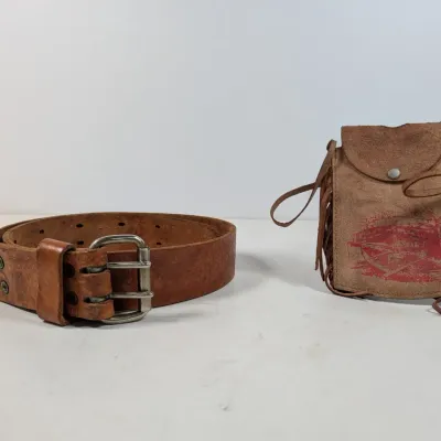Sale Photo Thumbnail #427: Vintage tan leather double-prong belt alongside a small suede fringed pouch featuring a printed graphic.