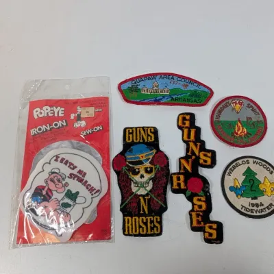 Sale Photo Thumbnail #410: Collection of vintage embroidered and iron-on patches, including Guns N' Roses band patches, Boy Scouts patches, and a packaged vintage Popeye iron-on.