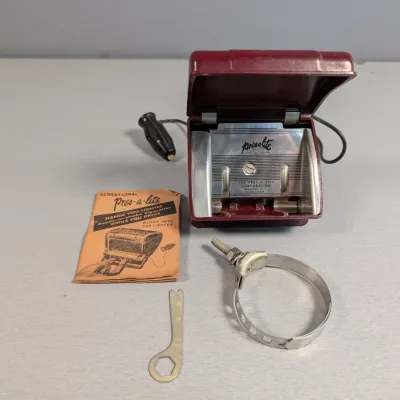Sale Photo Thumbnail #434: Vintage Pres-A-Lite automatic car cigarette dispenser and lighter set in burgundy plastic, including steering column clamp, tool, and original instruction pamphlet.