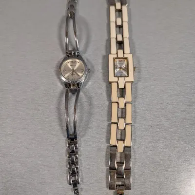 Sale Photo Thumbnail #143: Two women's quartz wristwatches, including a silver-tone openwork bangled watch and a rectangular-faced watch with cream enamel inlay details.