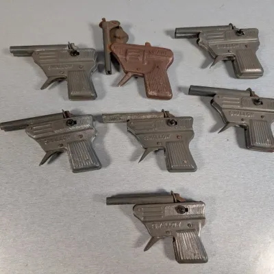 Sale Photo Thumbnail #310: Collection of seven vintage die-cast metal 'Swallow' toy cap guns, showing various degrees of patina and wear.