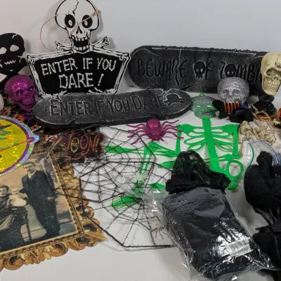 Sale Photo Thumbnail #41: Collection of Halloween decorations including skull signs, faux spider webs, glitter skulls, a green plastic skeleton, and various spooky wall hangings.
