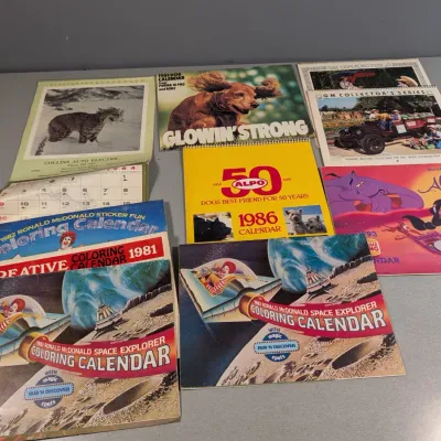 Sale Photo Thumbnail #22: Collection of vintage 1980s and 1990s wall calendars, including McDonald's coloring calendars, Disney's Aladdin, ALPO, and Purina calendars.