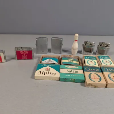Sale Photo Thumbnail #347: Collection of vintage lighters and novelty cigarette cases, including branded items from Tareyton, Pall Mall, Alpine, Salem, and Oasis.