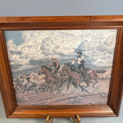 Sale Photo Thumbnail #331: Framed Western art print depicting cowboys riding horses and driving cattle under a stormy, lightning-filled sky, housed in a thick wood frame.