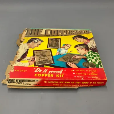 Sale Photo Thumbnail #225: Vintage mid-century "The Coppersmith" family hobby copper craft kit box, showing significant damage and wear to the left side.