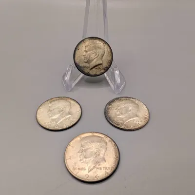Sale Photo Thumbnail #13: Group of four vintage US Kennedy half dollar coins, including 1964 and 1966 dates with light toning, one displayed on a clear plastic stand.