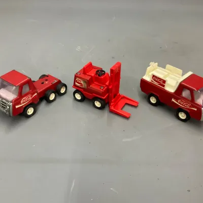 Sale Photo Thumbnail #279: Set of three vintage red Coca-Cola die-cast toy vehicles, including two delivery trucks and a forklift.