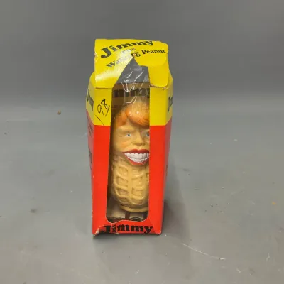 Sale Photo Thumbnail #242: Vintage 1970s Jimmy Carter "Jimmy the Walking Peanut" novelty wind-up toy, housed in its original worn packaging.