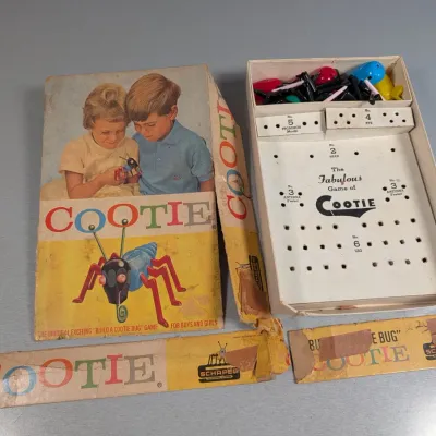 Sale Photo Thumbnail #353: Vintage Schaper 'The Fabulous Game of Cootie' board game with original box and colorful plastic game pieces, showing heavy wear and tape repairs on the box lid.