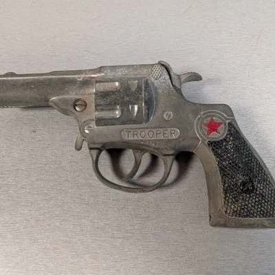 Sale Photo Thumbnail #312: Vintage Hubley 'Trooper' die-cast metal toy cap gun revolver with a red star emblem on the grip.