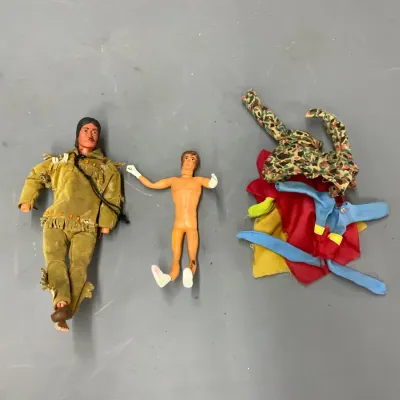 Sale Photo Thumbnail #402: Vintage action figures including a dressed Native American character, a bare male figure, and a small pile of doll clothing.