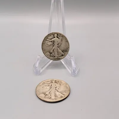 Sale Photo Thumbnail #16: Two 1942 Walking Liberty silver half dollars, with one coin displayed on a clear plastic easel stand.
