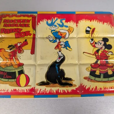 Sale Photo Thumbnail #339: Vintage lithographed tin Mickey Mouse Paint Box lid featuring Disney circus graphics of Pluto, Donald Duck, and Mickey Mouse, showing light age-related wear.