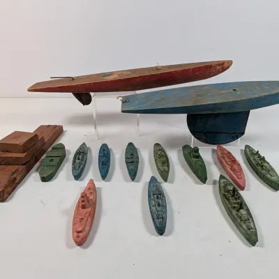 Sale Photo Thumbnail #419: Collection of vintage wooden boat toys, including two large hand-carved toy sailboat hulls and various small molded and carved ship miniatures with distressed paint finishes.
