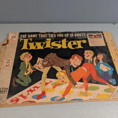 Sale Photo Thumbnail #451: Vintage 1960s Milton Bradley Twister board game box lid featuring classic illustrated cover art. The box displays heavy edge wear, taped corners, and creasing.