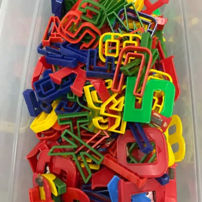 Sale Photo Thumbnail #297: Assortment of vintage colorful magnetic plastic letters stored in a clear plastic bin.