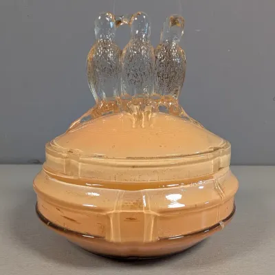 Sale Photo Thumbnail #118: Vintage Depression glass covered candy dish in peach opalescent tone, featuring three molded glass birds atop the lid as a finial.