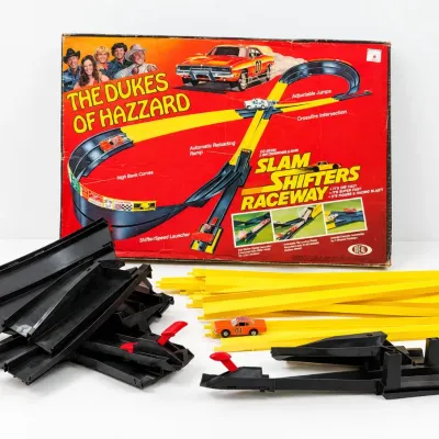 Sale Photo Thumbnail #420: Vintage 1981 Ideal Dukes of Hazzard Slam Shifters Raceway set, featuring original box art, plastic track pieces, and General Lee car.
