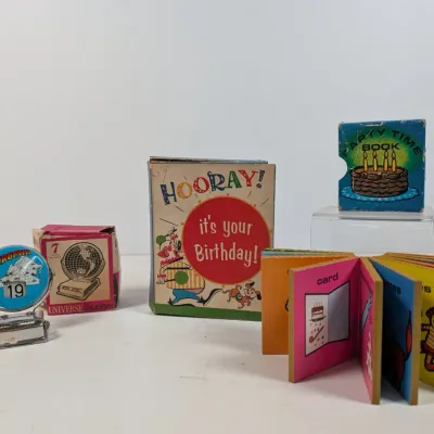 Sale Photo Thumbnail #411: Collection of vintage novelty items, including a metal desk flip calendar souvenir from Virginia, boxed Universe Calendar, and a mid-century "Hooray! It's Your Birthday!" miniature party book set.