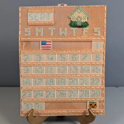 Sale Photo Thumbnail #29: Handcrafted plastic canvas needlepoint perpetual calendar featuring September decorations, including a small house, American flag, and jack-o'-lantern.