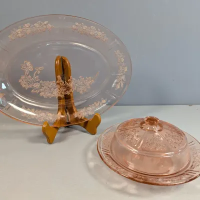 Sale Photo Thumbnail #176: Vintage pink Depression glass set featuring an etched oval platter on a stand and a covered butter dish with floral patterns.