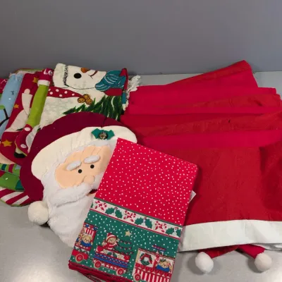 Sale Photo Thumbnail #154: Collection of holiday linens including Santa Claus chair back covers, various fabric Christmas stockings, and a patterned festive table runner.
