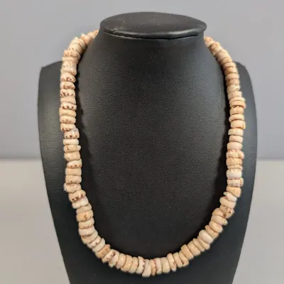 Sale Photo Thumbnail #322: Vintage puka shell necklace displayed on a black jewelry bust, featuring natural disc-shaped shell beads.