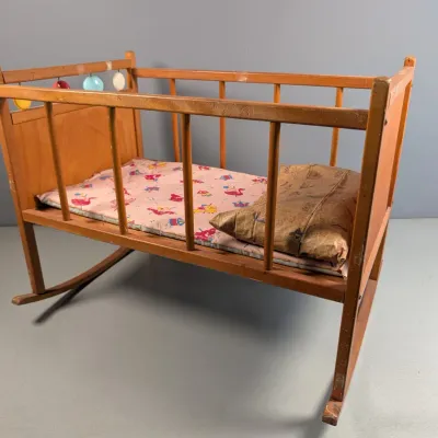 Sale Photo Thumbnail #326: Vintage wooden doll cradle featuring a rocking base, colorful attached beads, and patterned bedding.