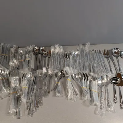 Sale Photo Thumbnail #155: Large collection of vintage stainless steel flatware and serving utensils, mostly wrapped in plastic bundles and organized by piece type.