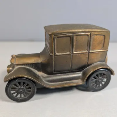 Sale Photo Thumbnail #369: Vintage brass Model T car figurine featuring black spoked wheels and a weathered patina.