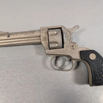 Sale Photo Thumbnail #315: Vintage Nichols Stallion 38 die-cast cap gun revolver with engraved silver-tone finish and textured black grips.