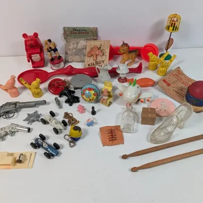 Sale Photo Thumbnail #390: Collection of vintage mid-century toys, novelties, and trinkets including cast metal cap guns, plastic figurines, miniature race cars, and drumsticks.
