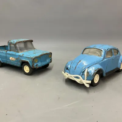 Sale Photo Thumbnail #280: Pair of vintage light blue pressed steel toy vehicles, including a pickup truck and a Volkswagen Beetle, both showing significant surface wear and patina.