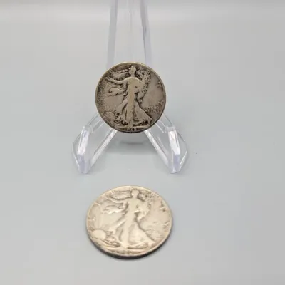 Sale Photo Thumbnail #14: Two United States Walking Liberty silver half dollars, including a 1938 issue displayed on a clear plastic stand.