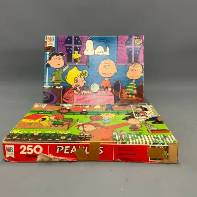 Sale Photo Thumbnail #105: Vintage Milton Bradley Peanuts 250-piece jigsaw puzzle featuring Snoopy, Charlie Brown, and friends. The box displays some shelf wear and tape, with a completed or sample picture set up behind it.