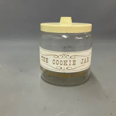 Sale Photo Thumbnail #282: Vintage clear glass cookie jar with a off-white lid and printed "THE COOKIE JAR" graphic, mid-20th century.