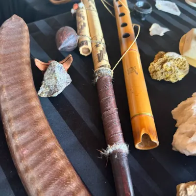 Collection of traditional wooden items including a curved instrument or boomerang, a leather-wrapped pipe, and a bamboo flute, displayed...