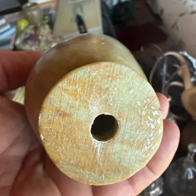 Underside of a carved stone or alabaster vessel showing a drilled central hole and natural yellow-green veining.