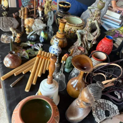 Eclectic assortment of tabletop decor, including wooden pan flutes, hand-carved figurines, ceramic vases, glass bells, and pottery.