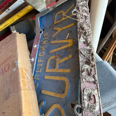 Vintage blue California personalized license plate reading "SURVYR" inside a dirt-covered license plate frame.