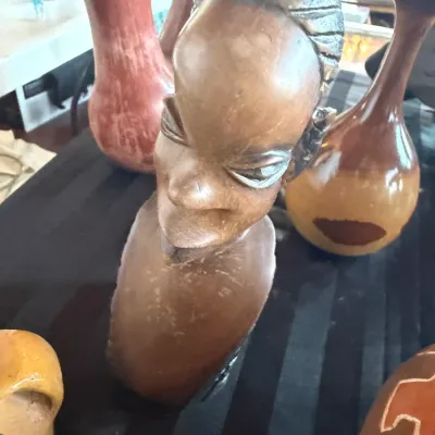 Hand-carved wooden African bust depicting a woman with braided hair, displayed alongside assorted ceramic vases.