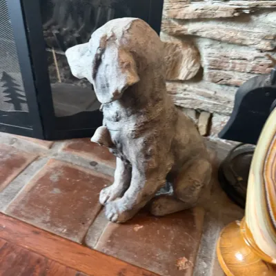 Cast concrete sitting dog statue, featuring a weathered finish and detailed collar, positioned near a stone fireplace hearth.
