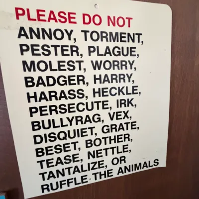 Novelty metal sign listing various synonyms for harassing animals, mounted on a wood surface.